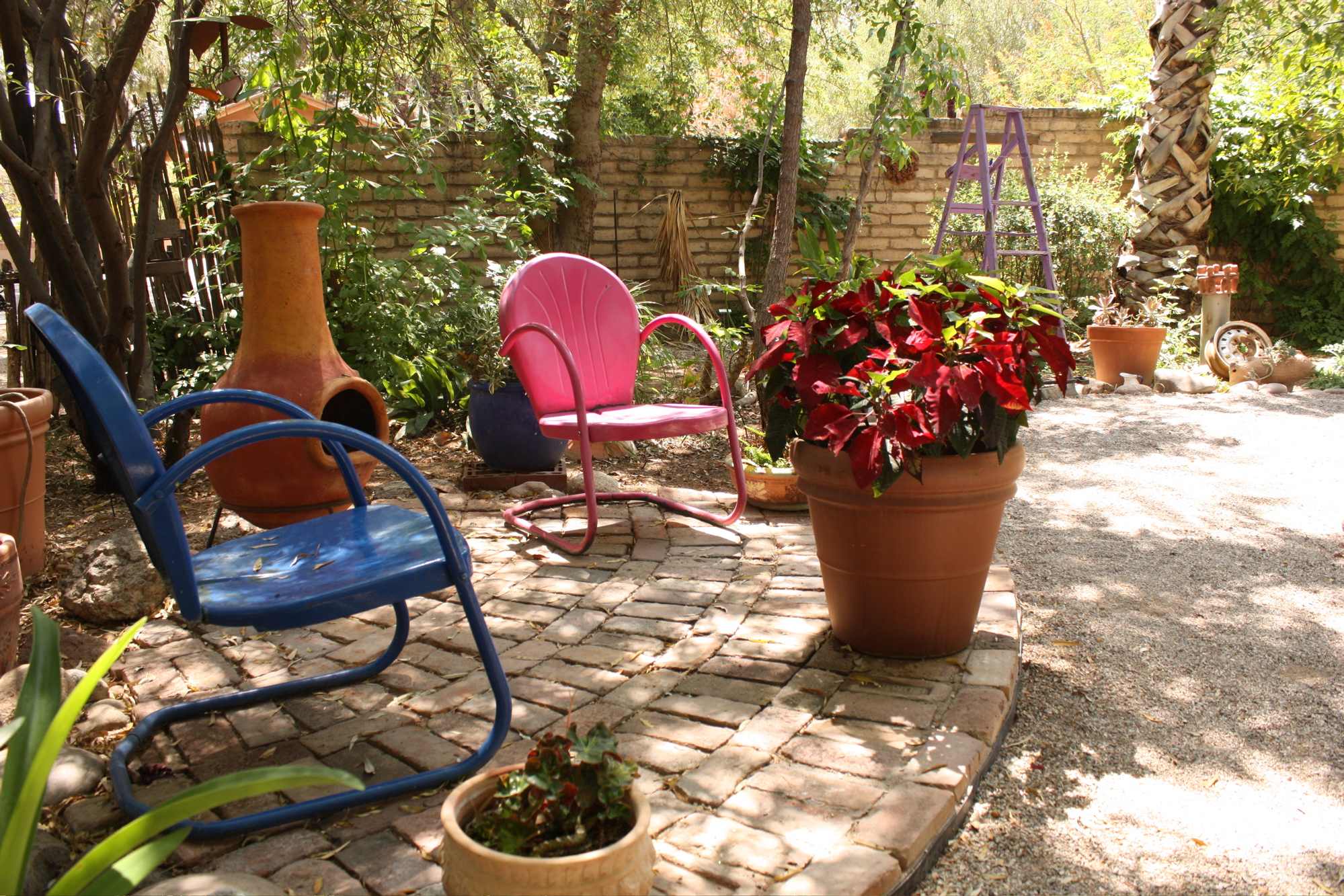 two colourful chairs and a pot of flowers in shade under trees. copyright JASoule